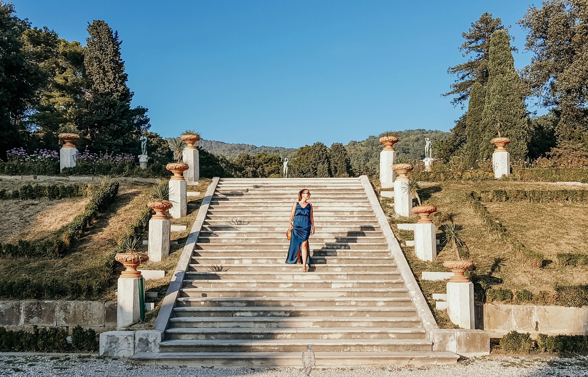 Front view of woman in long dress walking down stone stairs in park at Miramare, Trieste